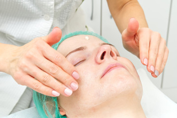 Beautician applies a natural moisturizing mask to the face of a young beautiful woman. Anti-aging...