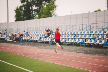 Woman Running At Stadium. Young woman running during on stadium track. Goal achievement concept. Fitness Jogging Workout on ballpark. Wellness theme. Sporty training cardio for weight loss success