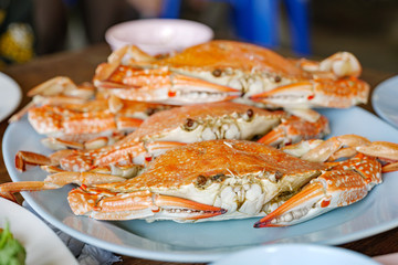 Heap of steamed fresh blue crabs serve on plate with spicy seafood sauce on side.