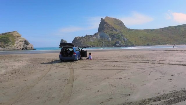 Tracking shot of a woman and blue van parked on the beach at Castlepoint in New Zealand