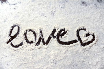 Word love and heart hand-painted on dark table covered with white flour, cooking for lover