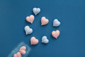 pink and blue meringue hearts in transparent glass goblet and are laid out in big heart on classic blue background diagonally, Valentines Day