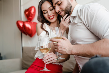 handsome couple man and woman drinking white wine from glasses at home sitting on couch