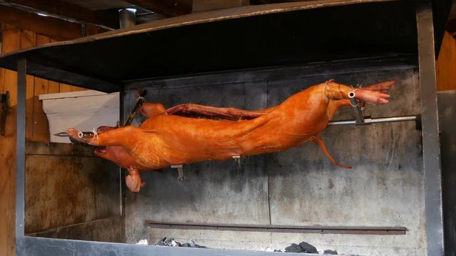 Big pig on a spit. Smoked and fried pig carcass at the medieval Christmas market in Munich. Whole roasted pork cooked with fire and charcoal, Food street festive of traditional European cuisine