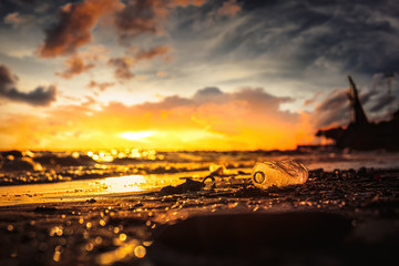 Plastic water bottle on the beach, environment pollution. Dirty beach and sunset.
