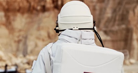 Rear of the spaceman in the white space costume with head armor walking the Mars or other unhabited planet. Back view. Close up. Outdoors.
