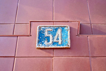 Number 54, fifty-four, blue plate on brown wall background.