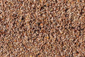 Small pebbles form the background of the sea shore. Coarse multicolor sand.