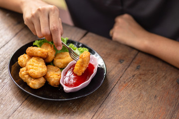 Chicken Nuggets impaled on a fork  and Dip sauce. A women eat Nuggets.