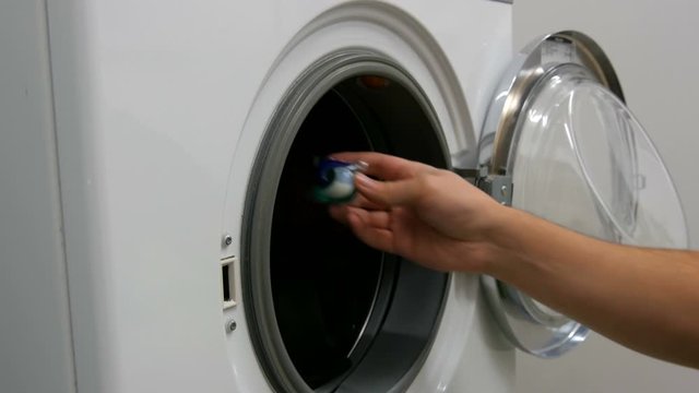 Male hands load a wash of colored laundry into a washing machine and place a capsule with washing powder. Expedited Shooting.
