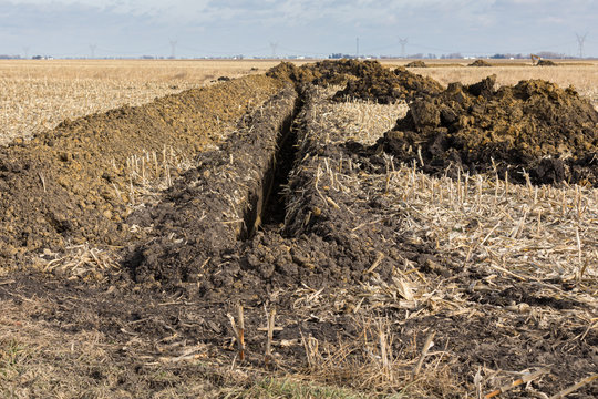 Trenck Excavated In Farm Field With Piles Of Soil. Water Drainage Pipe, Field Tile, Installation