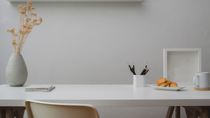 Close up view of workspace with copy space, decorations, stationery, coffee cup and croissant on white table with white wall