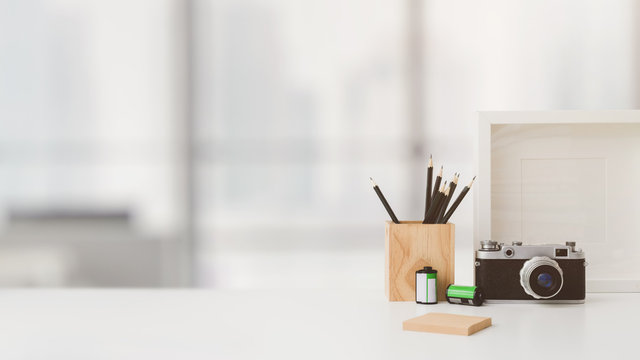 Cropped shot of workspace with copy space, camera, stationery, mock up frame, and tree pot on white table with blurred