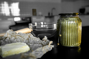 Ingredients and utensils for making cookies and cooking in the background of the kitchen. Yellow butter, baking paper, and sugar in a glass bowl on a black table.