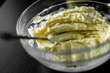 Soft butter with sugar in a glass mixing bowl with a fork. preparation of dough for cookies, cake and cakes. A black table and a jar of sugar.