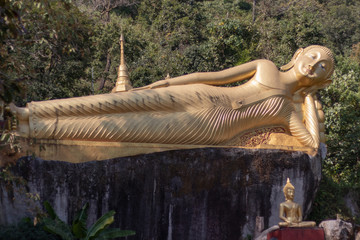 Golden reclining Buddha statue and two small meditation Buddha statues with trees around