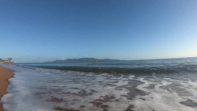 Small ocean waves breaking on the shore of a sandy beach in Townsville, with Magnetic Island in the background
