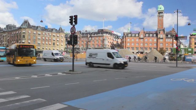 Cars crossing the street of Copenhagen, Denmark. Bikers crossing the street on a bicycle lane. A yellow bus turns right on the street.
