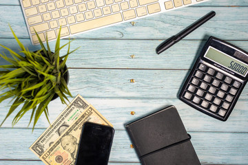 Finance Flat Lay - Conceptual. US Dollars, Calculator, keyboard, notebook, on blue wooden background