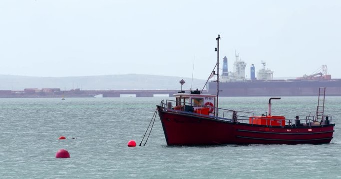 Floating boat ancored to an orange buoy in a sunny day. Industrial cargo dock on background, Cape Town South Africa