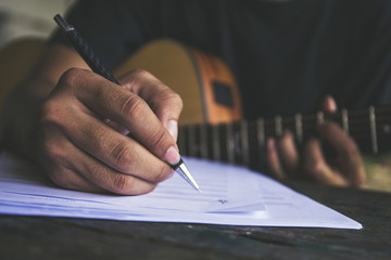 artist songwriter thinking writing notes,lyrics in book at studio.man playing live acoustic guitar...