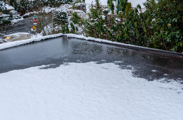 Flat carport roof covered in snow, slush, ice, and water, with clogged downspout drain, residential...