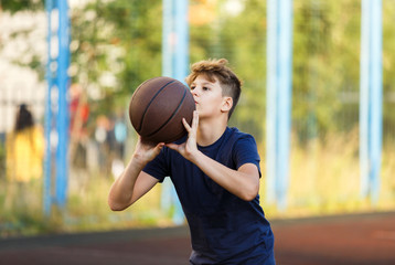 Cute boy in blue t shirt plays basketball on city playground. Active teen enjoying outdoor game with orange ball. Hobby, active lifestyle, sport for kids. 