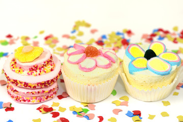 Three cute colorful cup cakes made of sugar and foam stand side by side against a white background and confetti with space for text