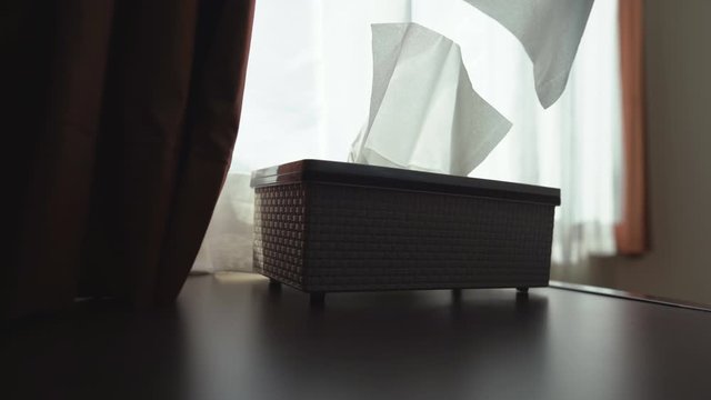 Close up hand pulling tissue paper in box on table, beside window bright light on white background, 