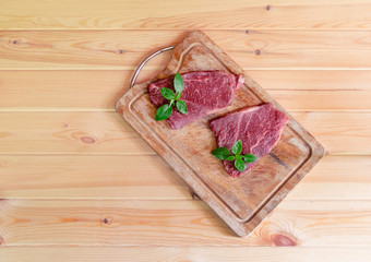 Raw fresh marbled meat Black Angus Steaks with fresh green basil on cutting board on wooden background. Selective focus.