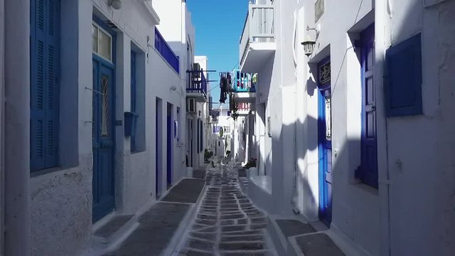 Point of view traveler dolly shot pushing down a clean alley way between whitewashed traditional Greek houses, shot on Mykonos island, Greece