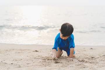 A boy is playing sand and swimming with his brother on the beach.