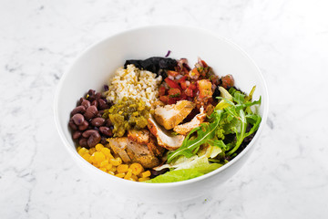Mexican Lunch bowl on marble background. Salad bowl with corn, red beans, tomato with red onion, jalapenios, chicken breast. Top view