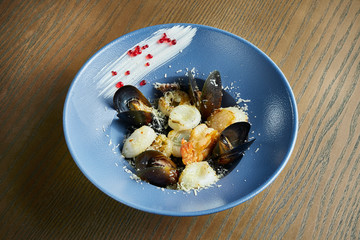 Traditional black risotto with seafood: tiger shrimp, scallops and mussels with parmesan and caviar in a blue bowl on a wooden background. Italian food