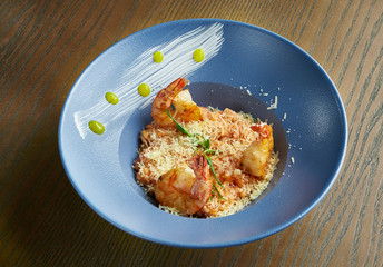 Homemade and fresh risotto with parmesan and shrimp. Italian traditional rice in a blue ceramic bowl on wooden background in. Close up view. Healthy seafood