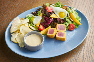Tasty Nicoise Salad served blue ceramic plate on wooden background. Close up view on salad with arugula, quail eggs, tomatoes and roasted tuna