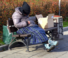 Auf einer Parkbank sitzender Obdachloser mit Decke 