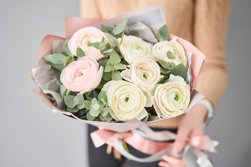 Obraz na płótnie Canvas Persian buttercup in womans hands. Bunch pale pink ranunculus flowers with green eucalyptus. The work of the florist at a flower shop