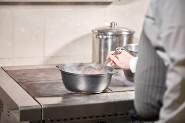 chef cook adds the ingredients. traditional beef broth with vegetable, bones and ingredients in pot, cooking recipe. Soup in a cooking pot with ladle on dark stone background. Top view