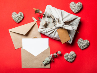 Zero waste Valentine's Day concept and mock up on red. Eco-friendly gift cloth wrapping in Furoshiki style, craft paper envelope,empty greetings card. Top down view or flat lay. Copy space for design