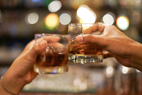 two men clinking glasses of whiskey drink alcohol beverage together at counter in the pub 