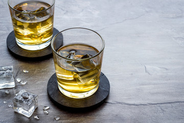 Whiskey near ice cubes on grey stone background copy space