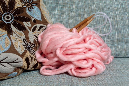 Skein Of Giant Merino Pink Yarn For Arm Knitting With Large Knitting Needles On A Blue Sofa