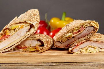 Shawarma chicken roll in a pita with fresh vegetables and cream sauce on wooden background. Selective focus