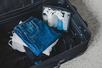 travel essentials and packing light for a holiday concept, luggage with pile of clothes next to transparent liquid bag for airport security screening compliance