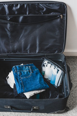 Naklejka premium packing light for a holiday concept, luggage with pile of clothes next to transparent liquid bag for airport security screening compliance