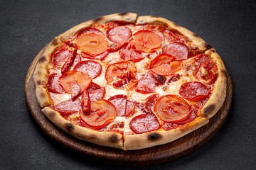 Italian Cuisine. Pepperoni pizza with salami sausage and red hot pepper, lies on a wooden board, on a black background. background image, copy space text