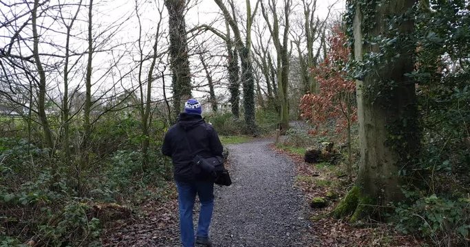Person in coat and hat walking through woodlands path in the woods