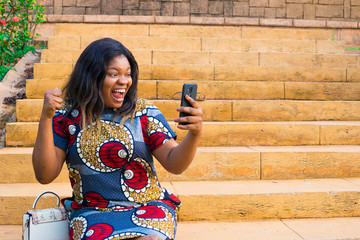 young african lady viewing something on her phone, feeling excited, celebrating and happy