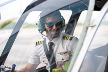 Confident smiling pilot wearing ear muff sitting in cockpit - obrazy, fototapety, plakaty